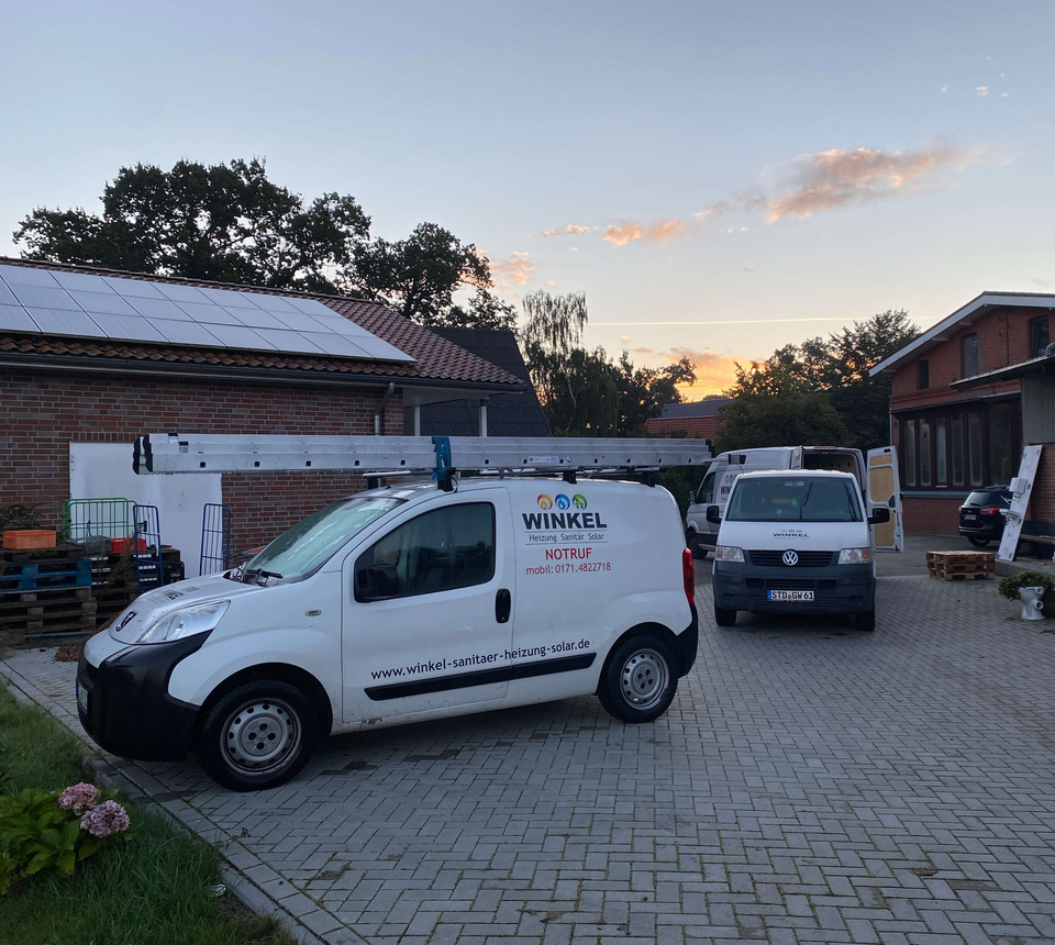 Zwei Firmenfahrzeuge der Winkel GmbH (Heizung, Sanitär, Solar) parken vor dem Betriebsgebäude mit Photovoltaikanlage auf dem Dach bei Sonnenuntergang.