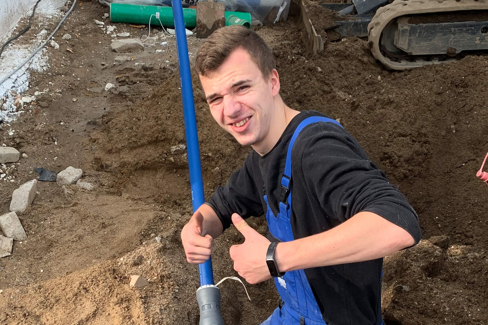Auszubildender Justin Kunde der Winkel GmbH zeigt Daumen hoch auf einer Erdbaustelle mit Rohrleitungen.