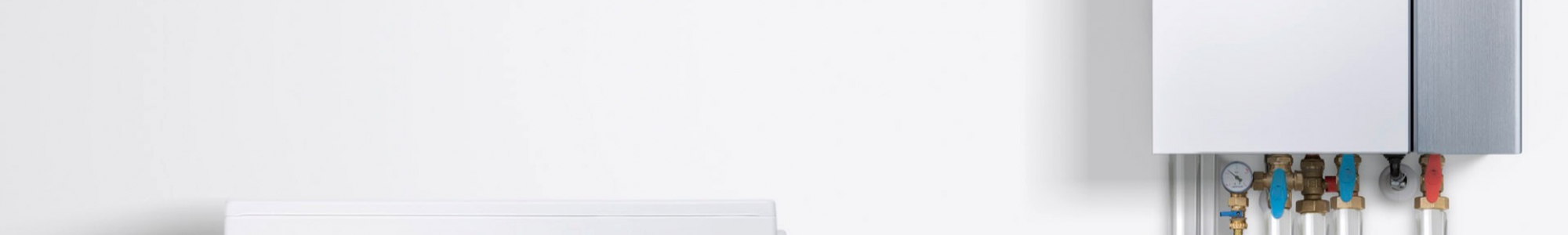 Außeneinheit einer Wärmepumpe neben einem Heizungsverteiler mit Rohrleitungen und Armaturen