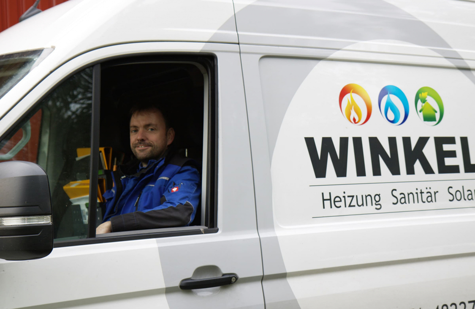 Thomas Winkel sitzt lächelnd am Steuer des Firmentransporters mit Logo und Aufschrift Heizung, Sanitär, Solar.